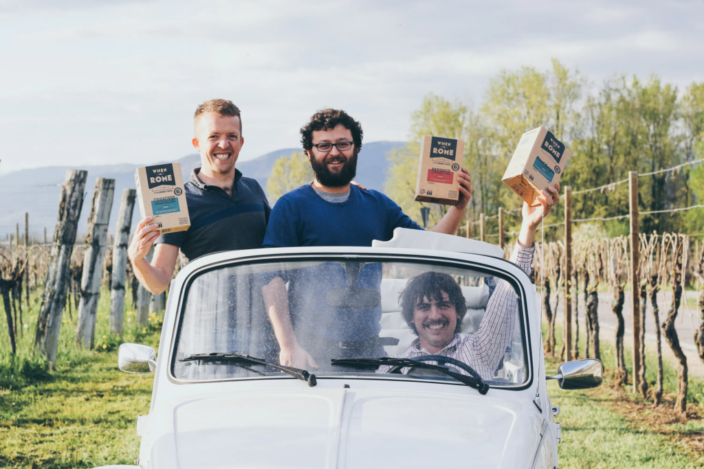 Three men in Italy holding boxes of When in Rome wine